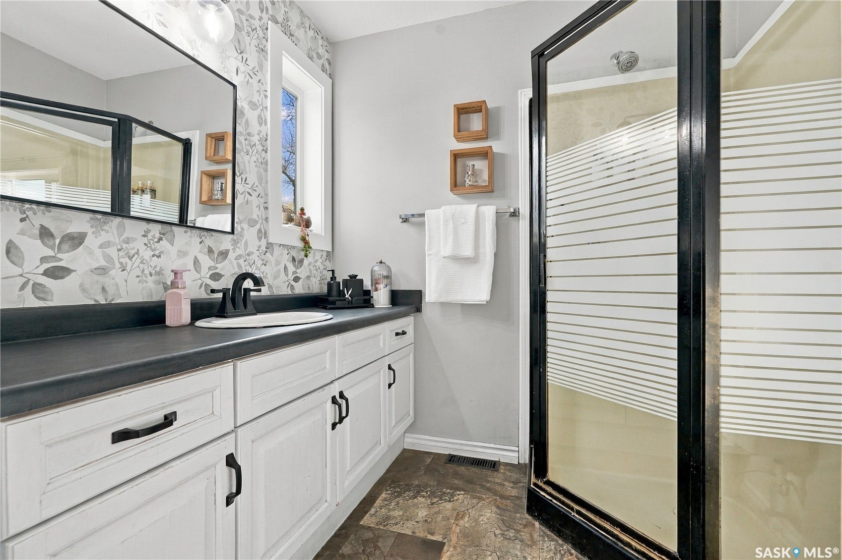White vanity with black hardware, dark countertop, single basin sink, matte black faucet, and framed mirror