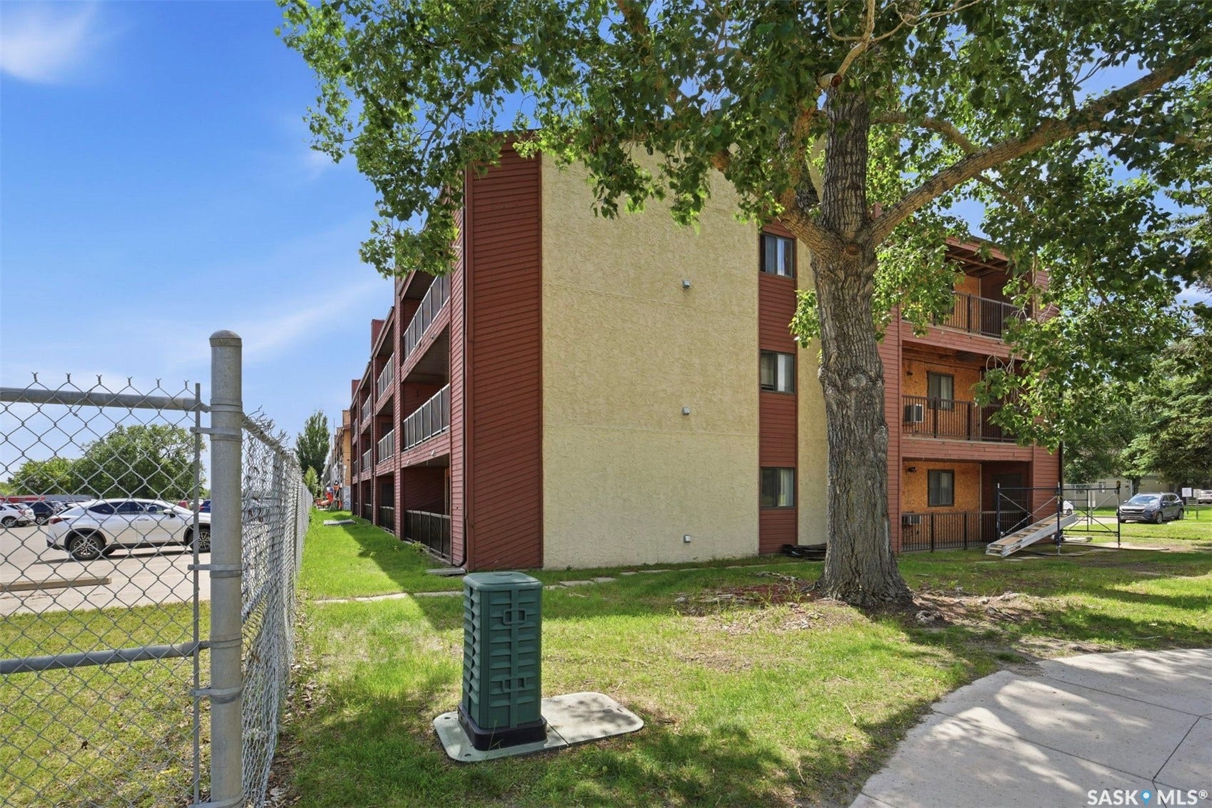 Multi-story building featuring textured beige and red siding, individual balconies with black railings, and multiple window units