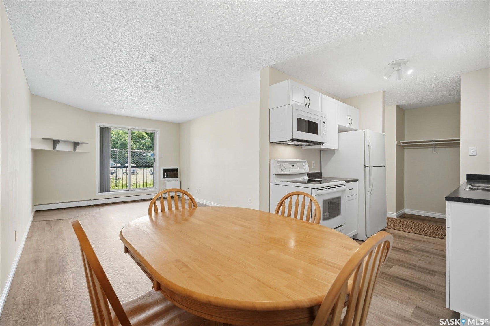 Open-concept living space featuring wood-finish flooring, white cabinetry, track lighting, and a sliding glass door