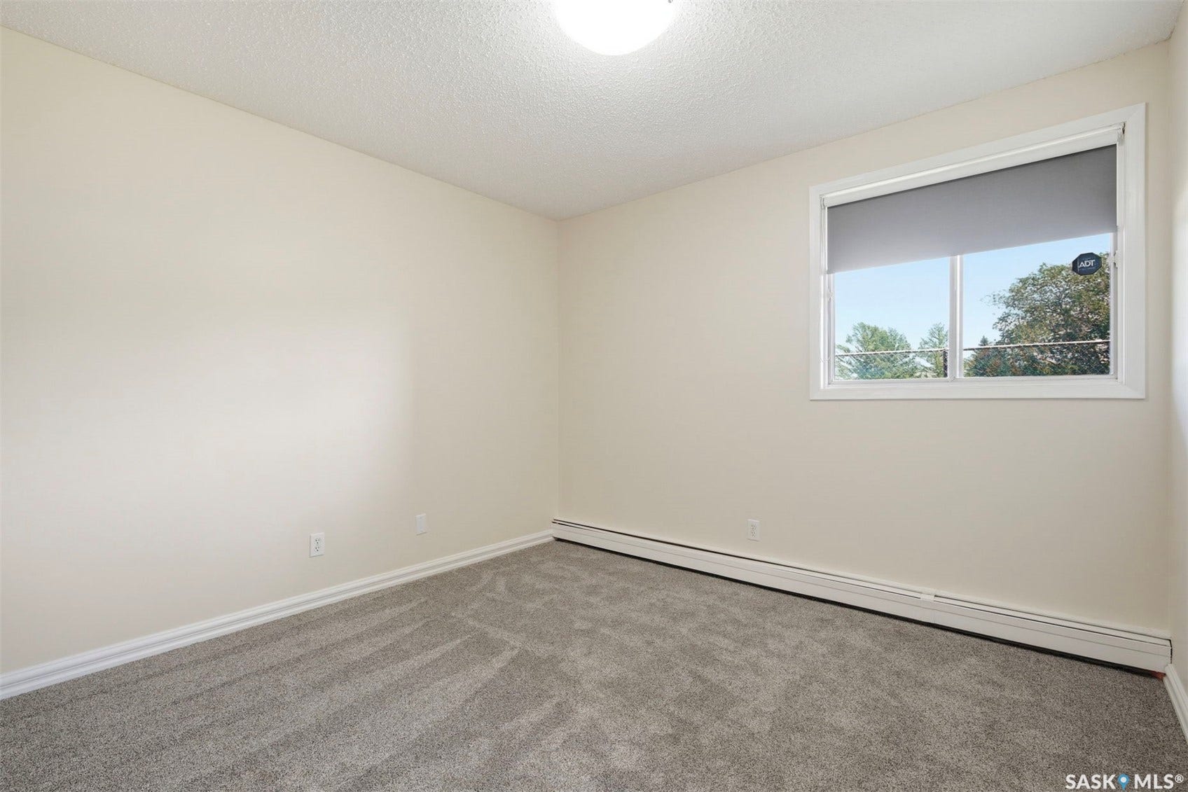 Neutral-toned wall paint, textured ceiling, gray carpet flooring, and a single window with a blind