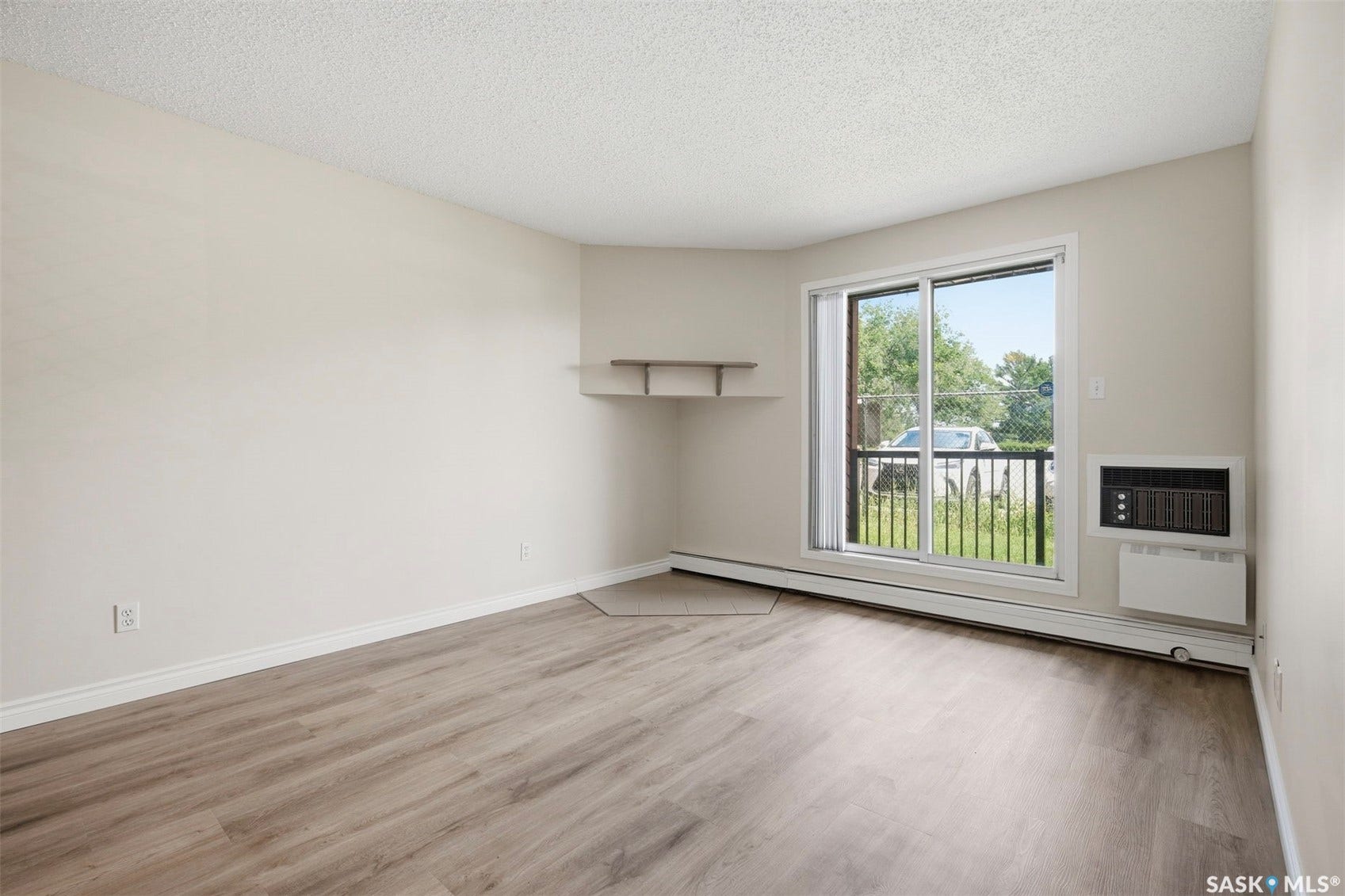 Wood-finish flooring, light neutral wall paint, corner shelving, sliding glass door, and wall-mounted air conditioning unit