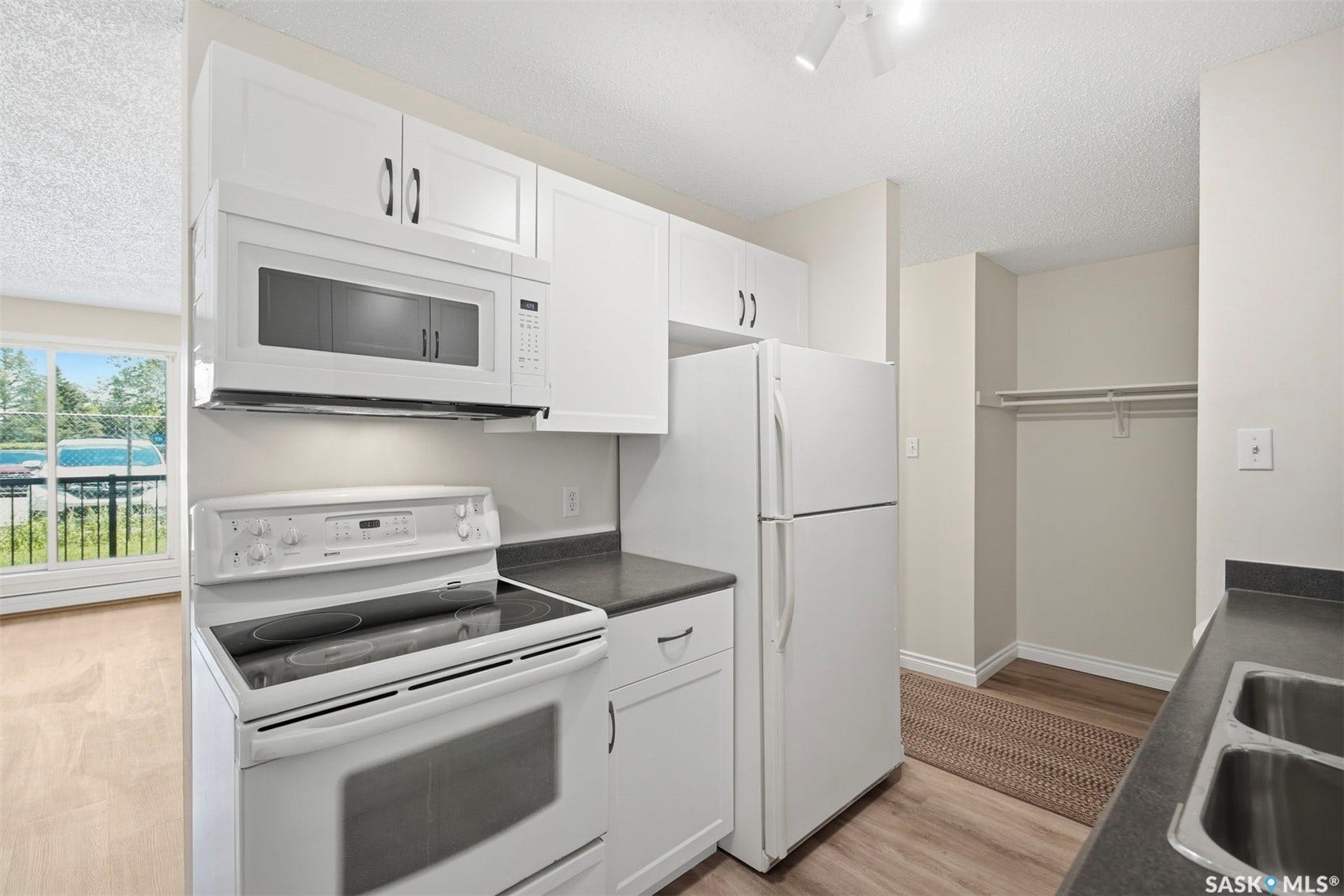 Kitchen featuring white cabinetry, dark countertops, a double basin stainless steel sink, and wood-finish flooring