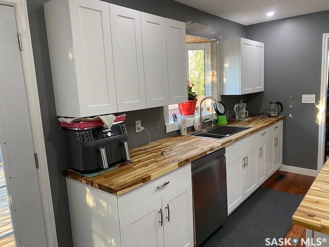 216 2nd Avenue, Wiseton SK S0L 3M0 White shaker cabinetry with dark hardware, wood-finish countertops, stainless steel dishwasher, undermount sink with gooseneck faucet, and recessed ceiling lighting