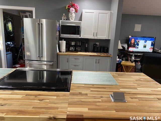 216 2nd Avenue, Wiseton SK S0L 3M0 Wood-finish island countertop with built-in cooktop, stainless steel refrigerator, and light-toned cabinetry