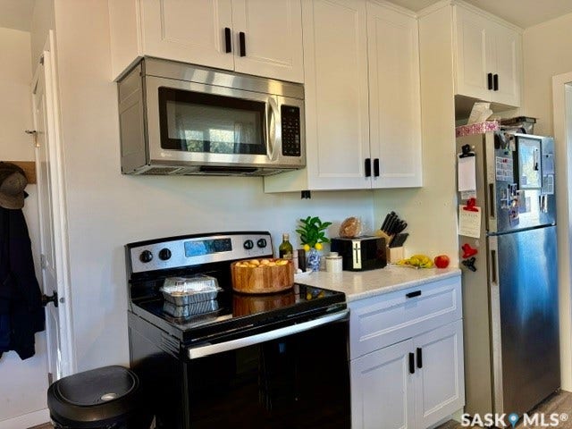 Stainless steel refrigerator, stainless steel over-the-range microwave, white cabinetry with dark hardware, black electric range, and light-toned countertops