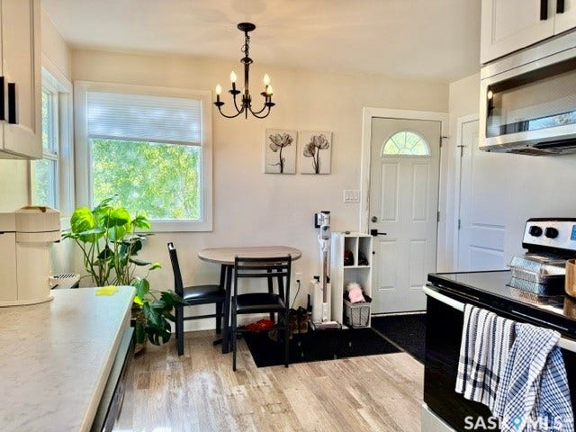 vinyl plank flooring, white cabinetry with dark hardware, a window with a pleated shade, and a black chandelier