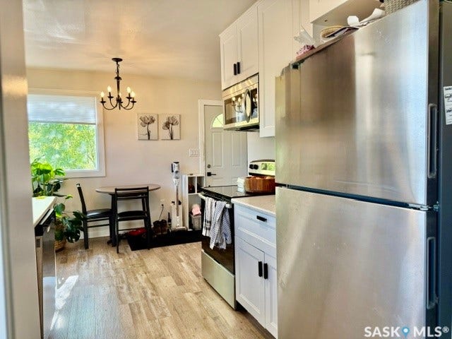 Contemporary kitchen featuring stainless steel appliances, white cabinetry with black hardware, vinyl plank floors, and a window with blinds