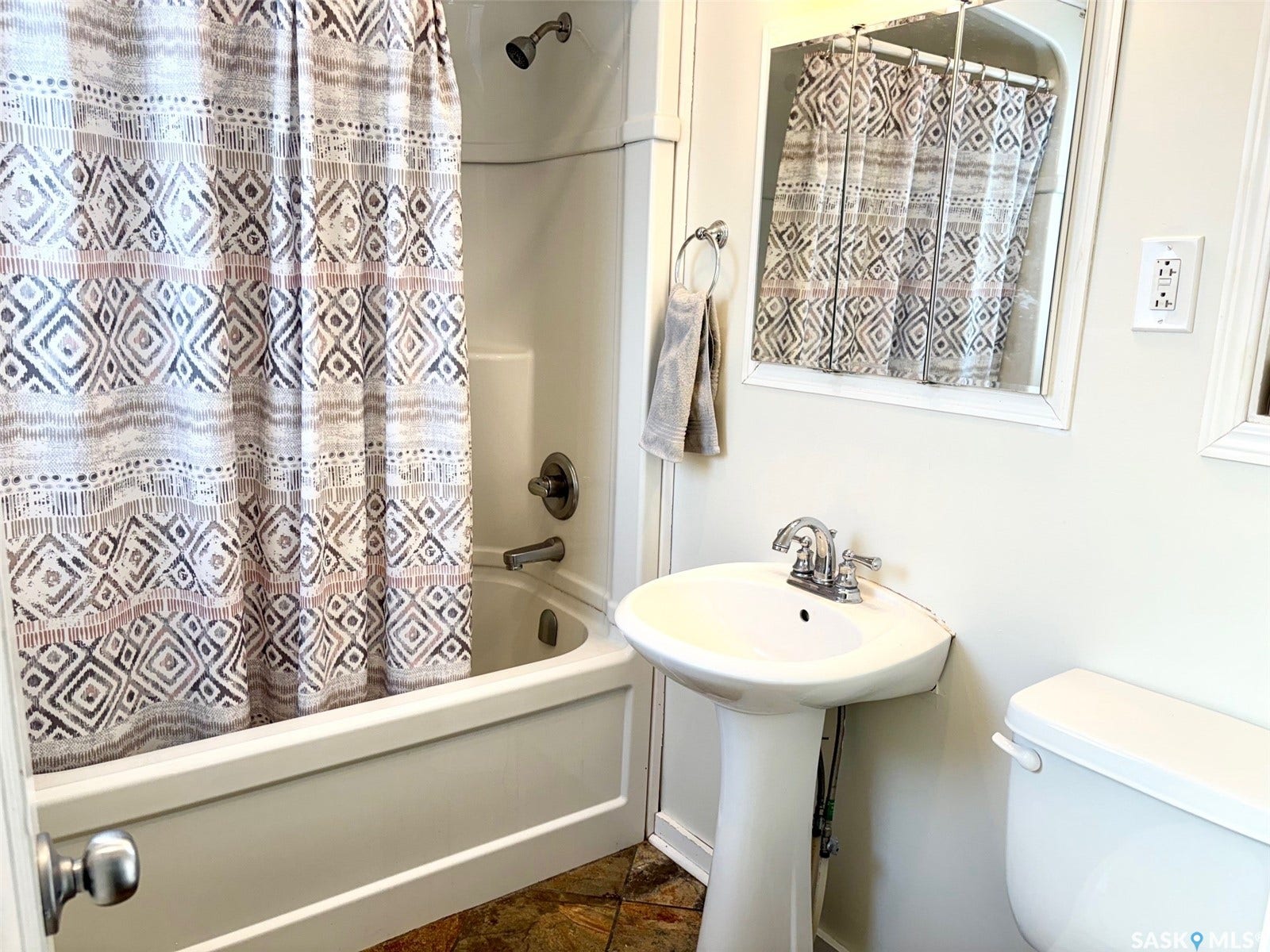 Pedestal sink with chrome faucet, toilet, and a white bathtub with a shower fixture
