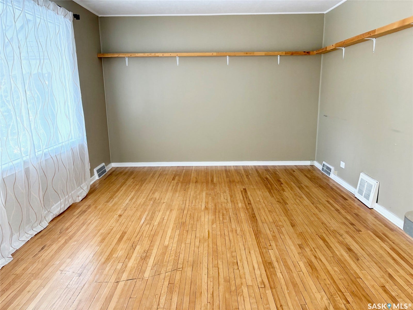 Hardwood flooring throughout, neutral wall color, and a window with sheer curtains