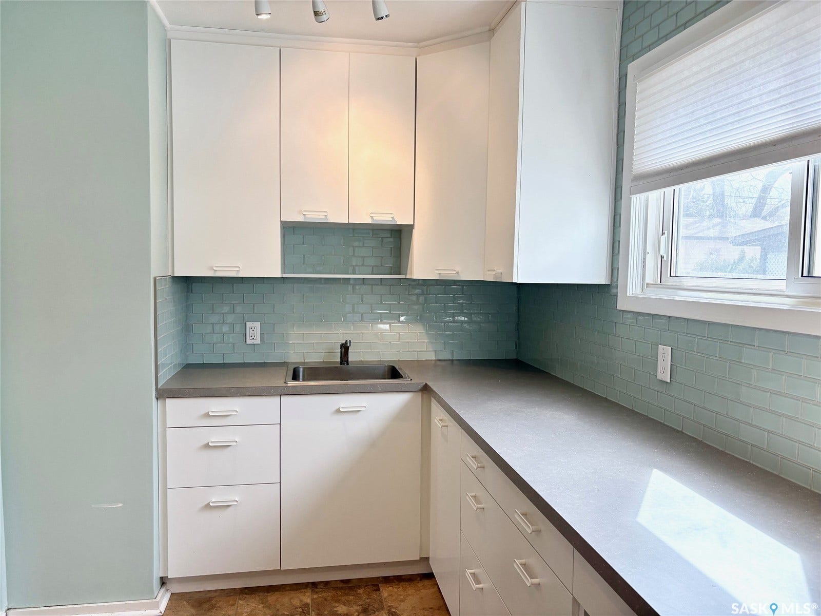 White cabinetry with integrated hardware, gray countertops, and a blue subway tile backsplash