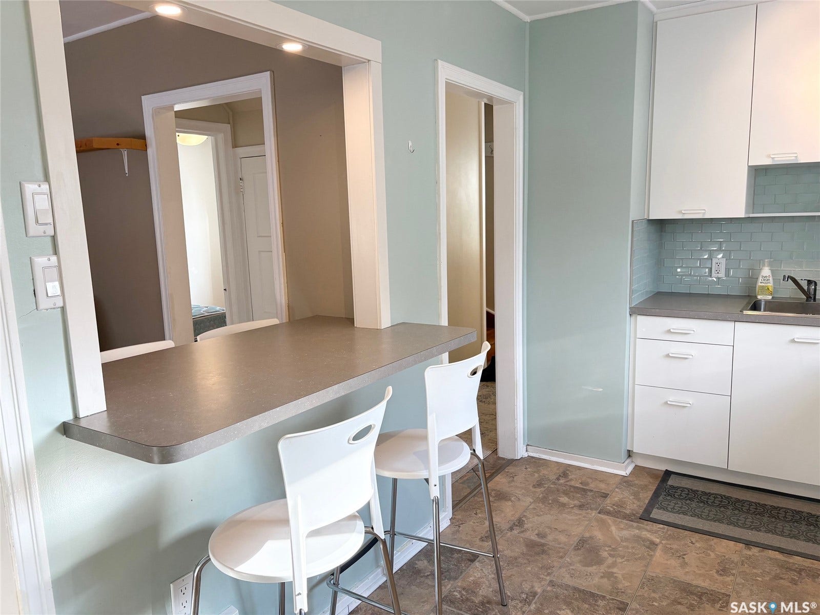 Kitchenette featuring a pass-through counter, white cabinetry, light blue subway tile backsplash, and a stainless steel sink