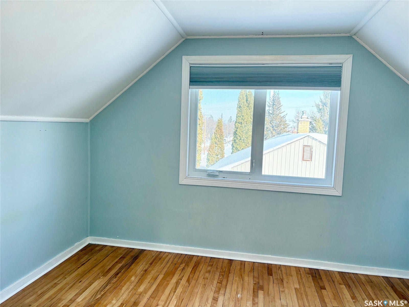 Wood-finish flooring with white trim, a window with horizontal blinds, and sloped ceiling