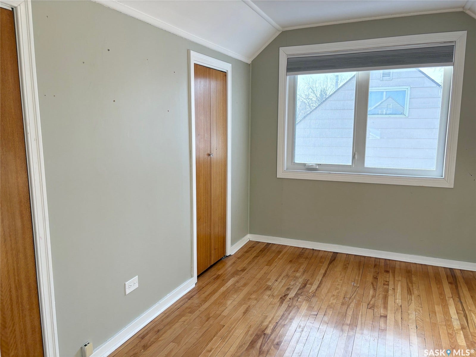 Hardwood flooring, painted walls, white trim, wood-finish doors, and a window with a roller shade
