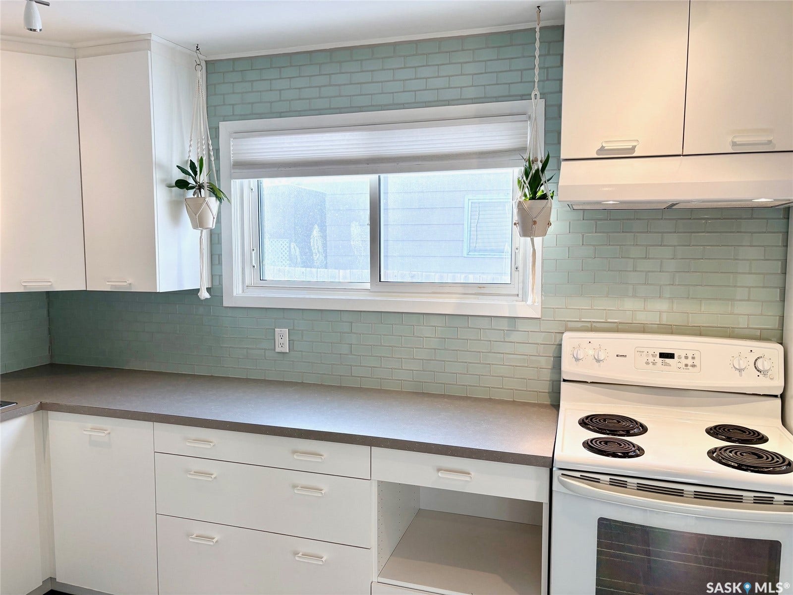 Crisp white cabinetry paired with a soft green subway tile backsplash and dark countertops