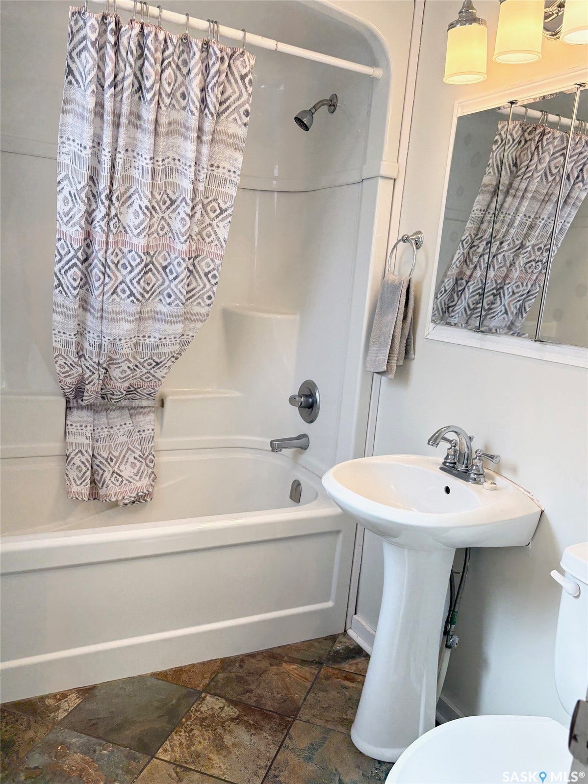 White pedestal sink with chrome faucet, complemented by a large wall mirror and three-light vanity fixture