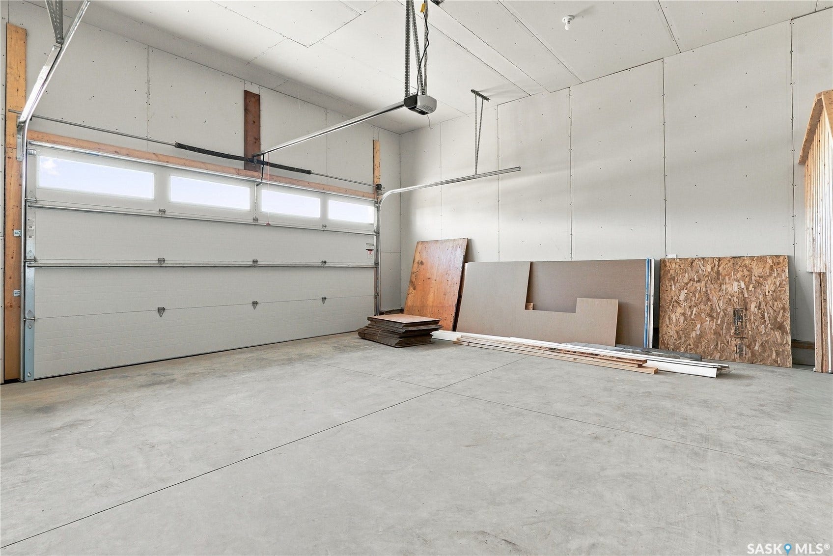 Concrete flooring, white panel garage door, upper garage door window panels, drywall-finished interior walls, and an automatic garage door opener