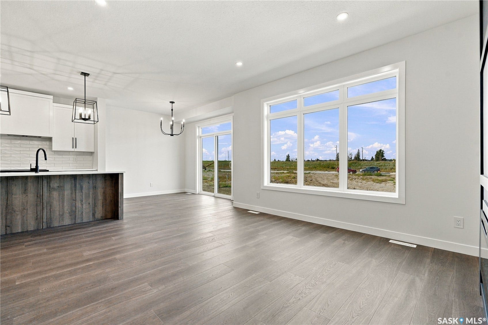 Wood-finish flooring, recessed lighting, white kitchen cabinetry with matte black hardware, kitchen island with a quartz countertop, and large windows