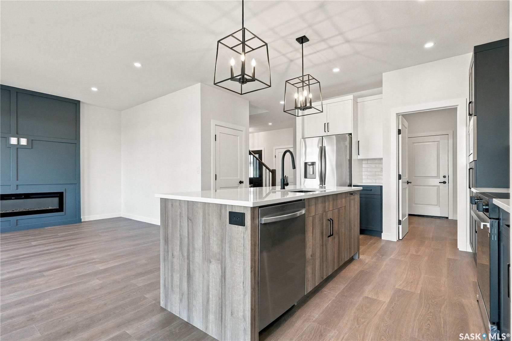 Open-concept kitchen and living area featuring wood-finish flooring, a kitchen island with integrated sink, stainless steel appliances, and a wall-mounted fireplace