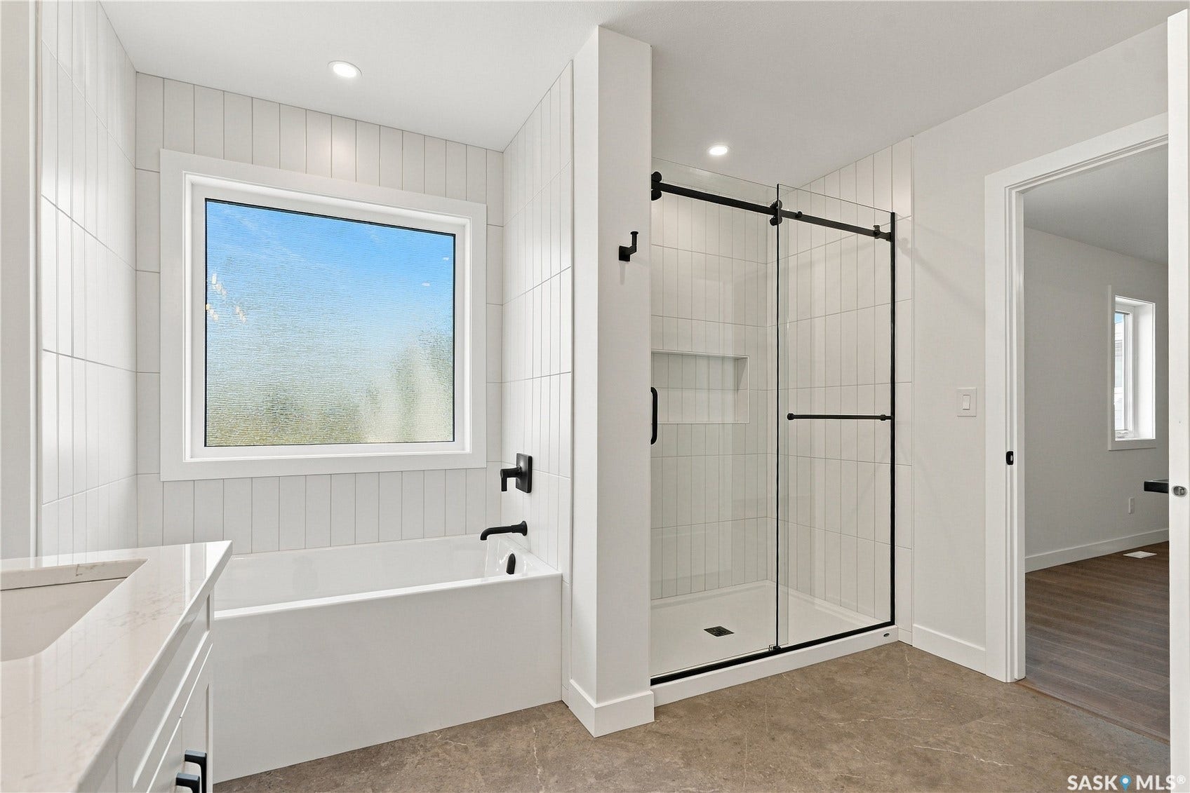 White subway tile wall accents, a built-in soaking tub with matte black fixtures, and a glass-enclosed shower with black framing