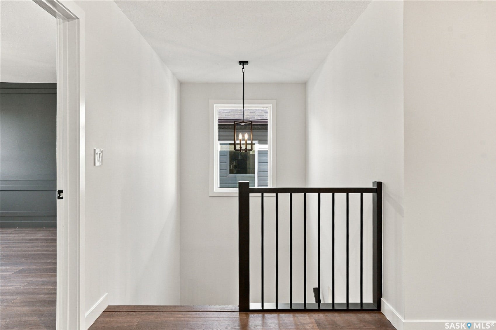 Recessed window with a black-framed pendant light, wood-finish flooring, and a dark wood and metal stair railing