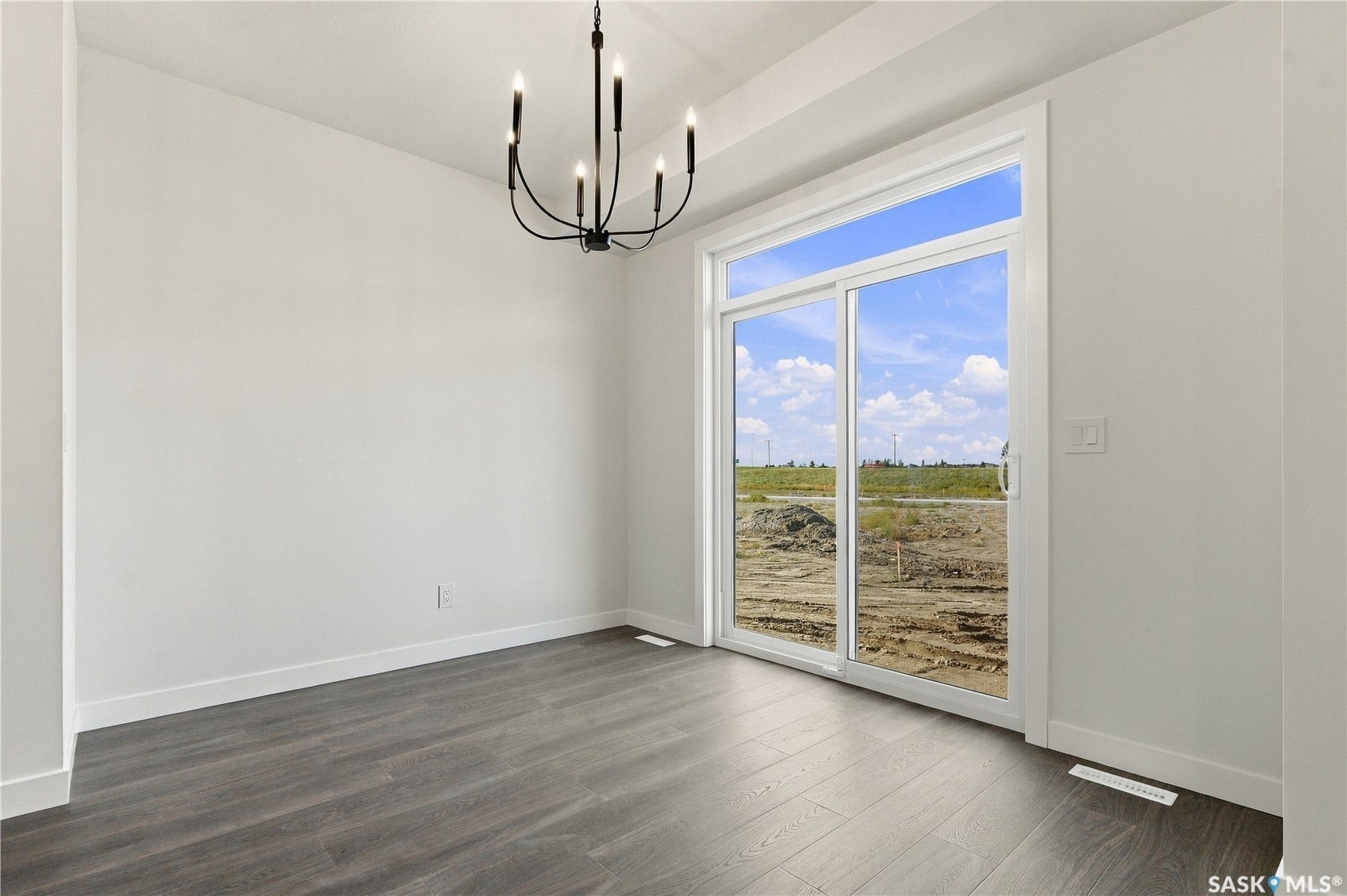 Sliding glass door, wood-finish flooring, white walls, and a black chandelier