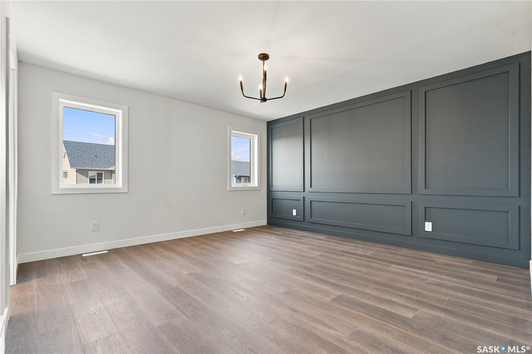 Wood-finish flooring, accent wall with decorative molding, two windows, and a multi-arm chandelier