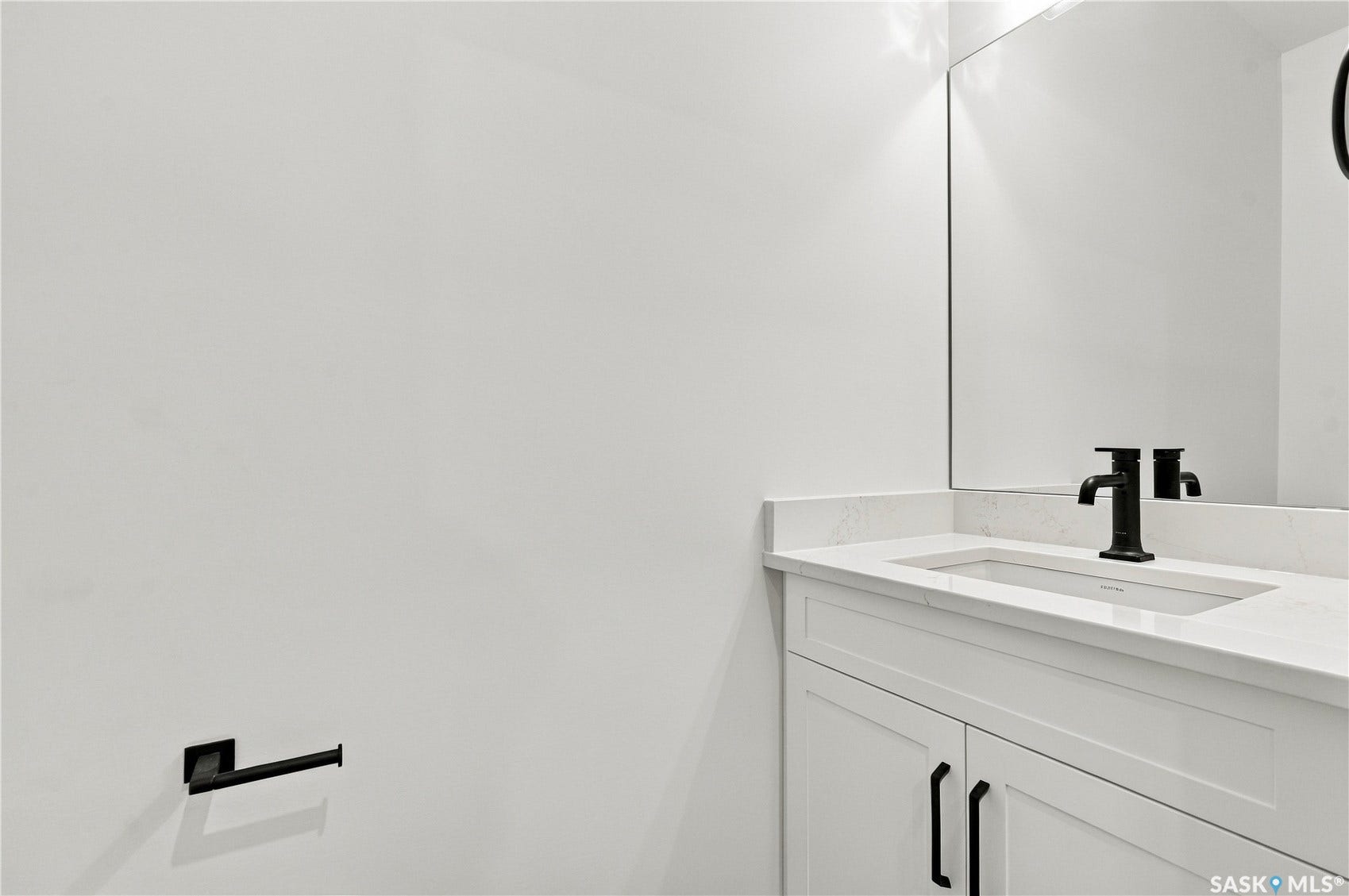 White vanity with shaker-style cabinetry, matte black hardware, integrated rectangular sink, and light countertop