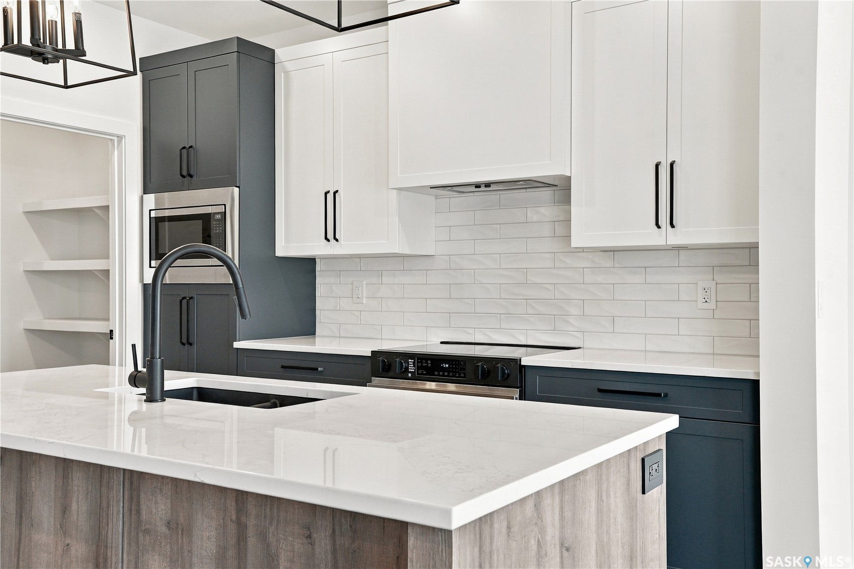 Modern kitchen featuring a large island with a composite countertop, two-tone cabinetry, stainless steel appliances, a subway tile backsplash, and a built-in microwave