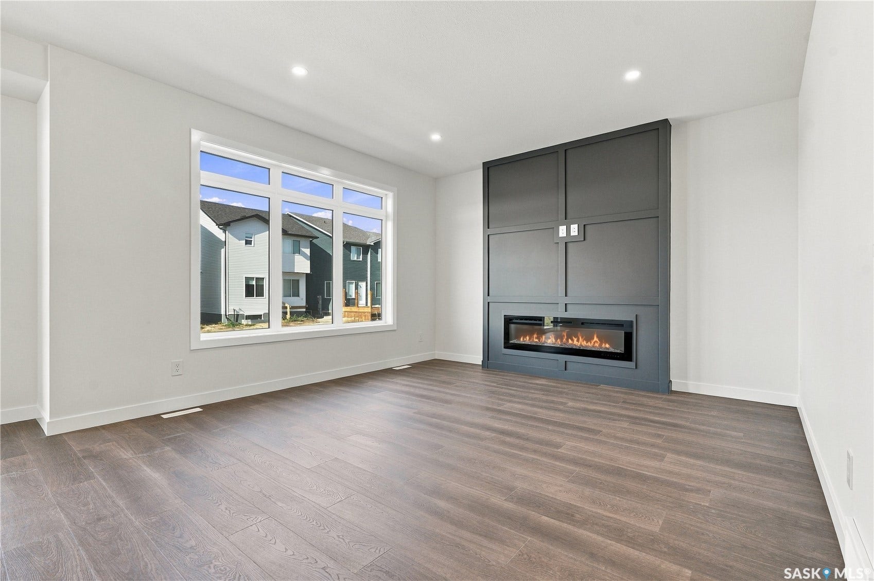 Spacious room featuring wood-finish flooring, a large multi-pane window, and a built-in electric fireplace with custom paneling