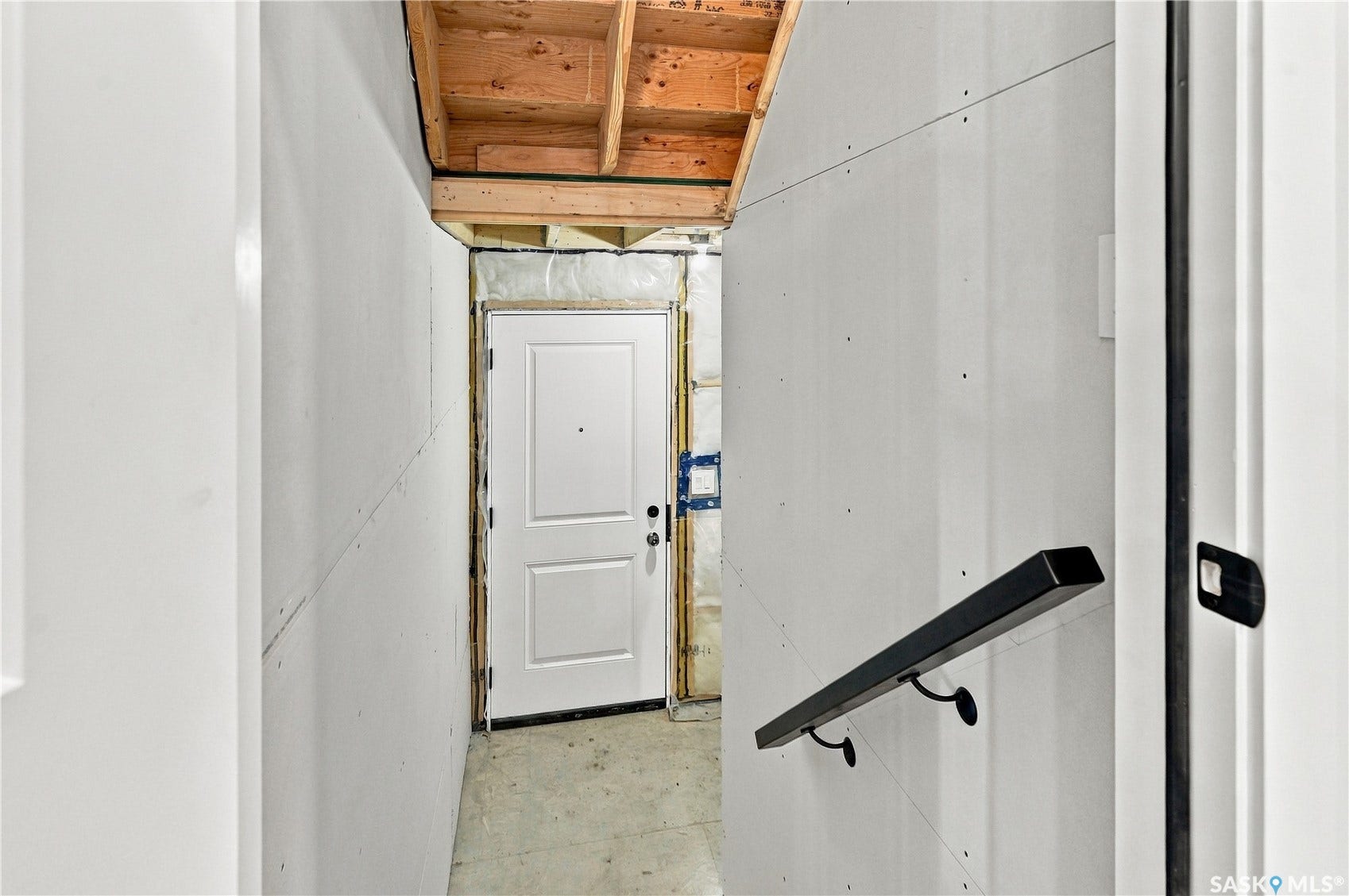 Unfinished walls, exposed ceiling joists, and a white paneled door