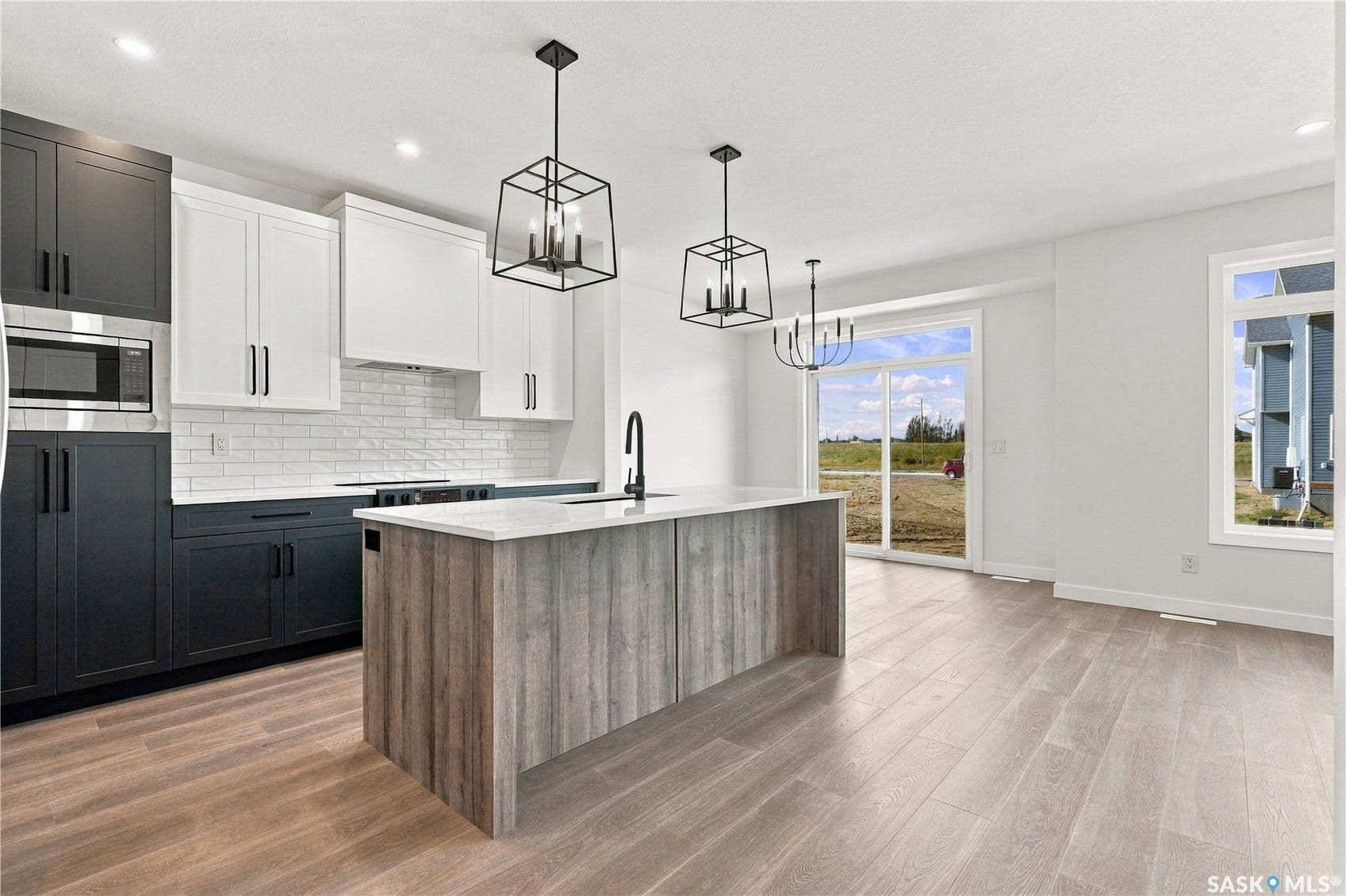 Modern kitchen featuring two-tone cabinetry, white subway tile backsplash, a center island with a light-toned wood-finish base, and pendant lighting