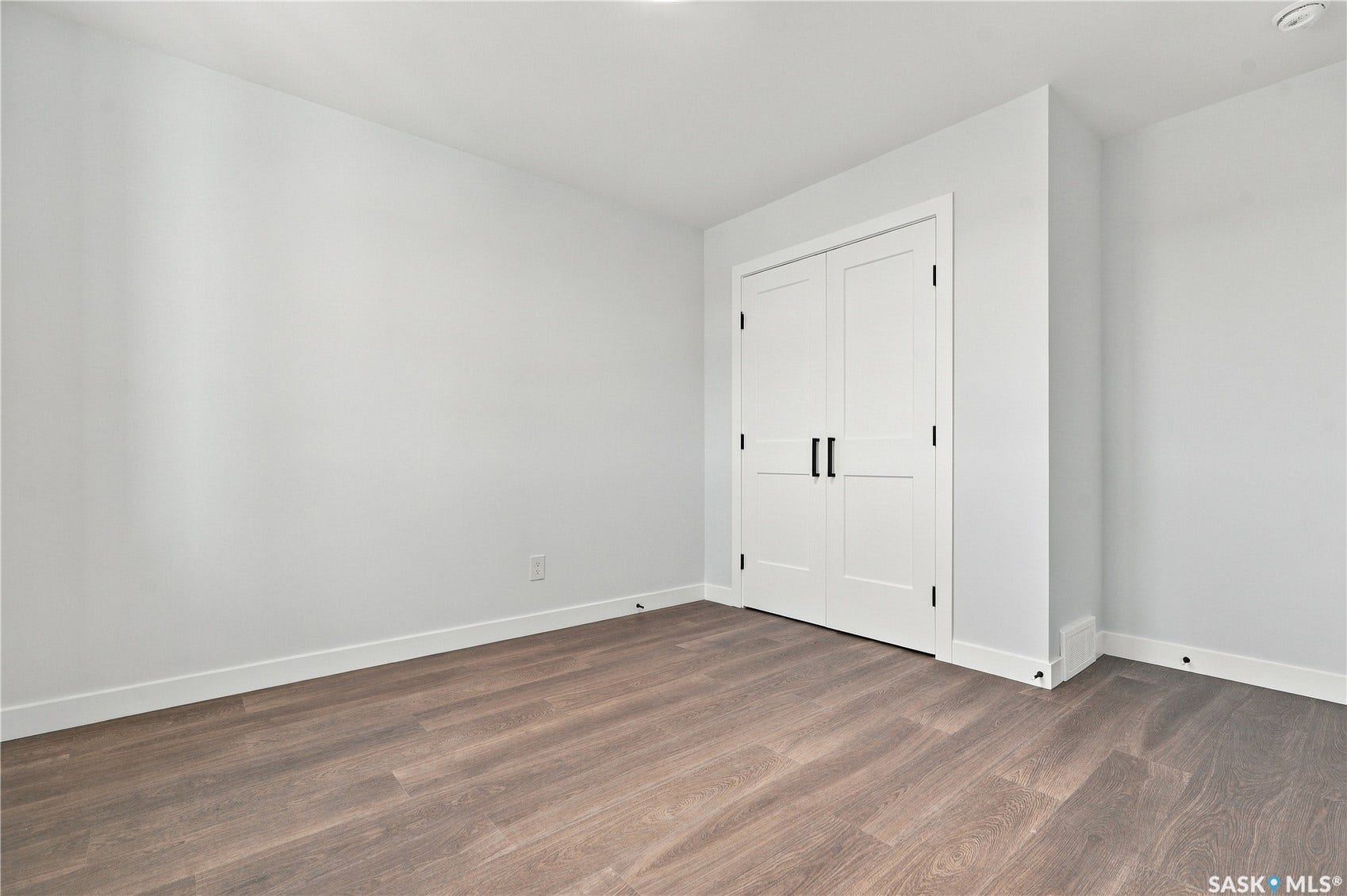 Neutral wall paint, wood-finish flooring, white trim, and bi-fold closet doors with black hardware