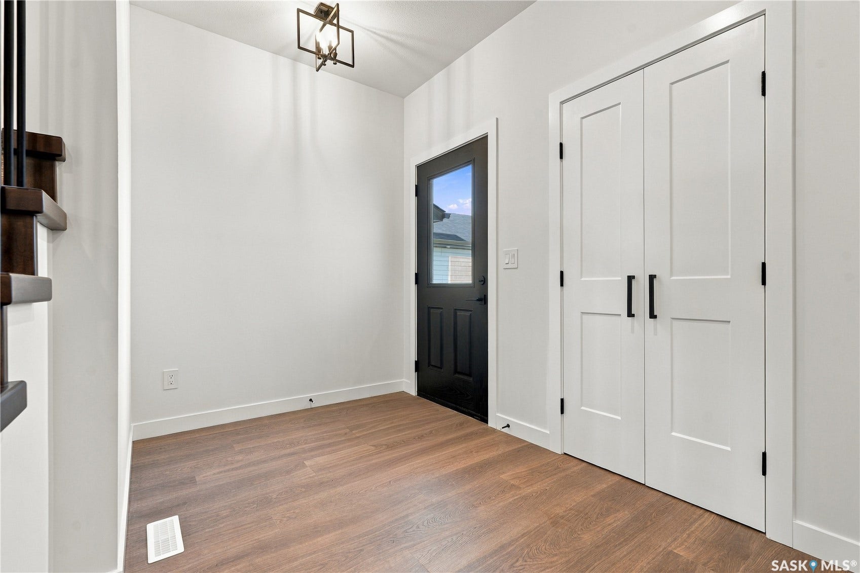 Hardwood-finish flooring, white walls, black frame door with glass insert, white double panel doors with black hardware, and an overhead bronze-finish light fixture