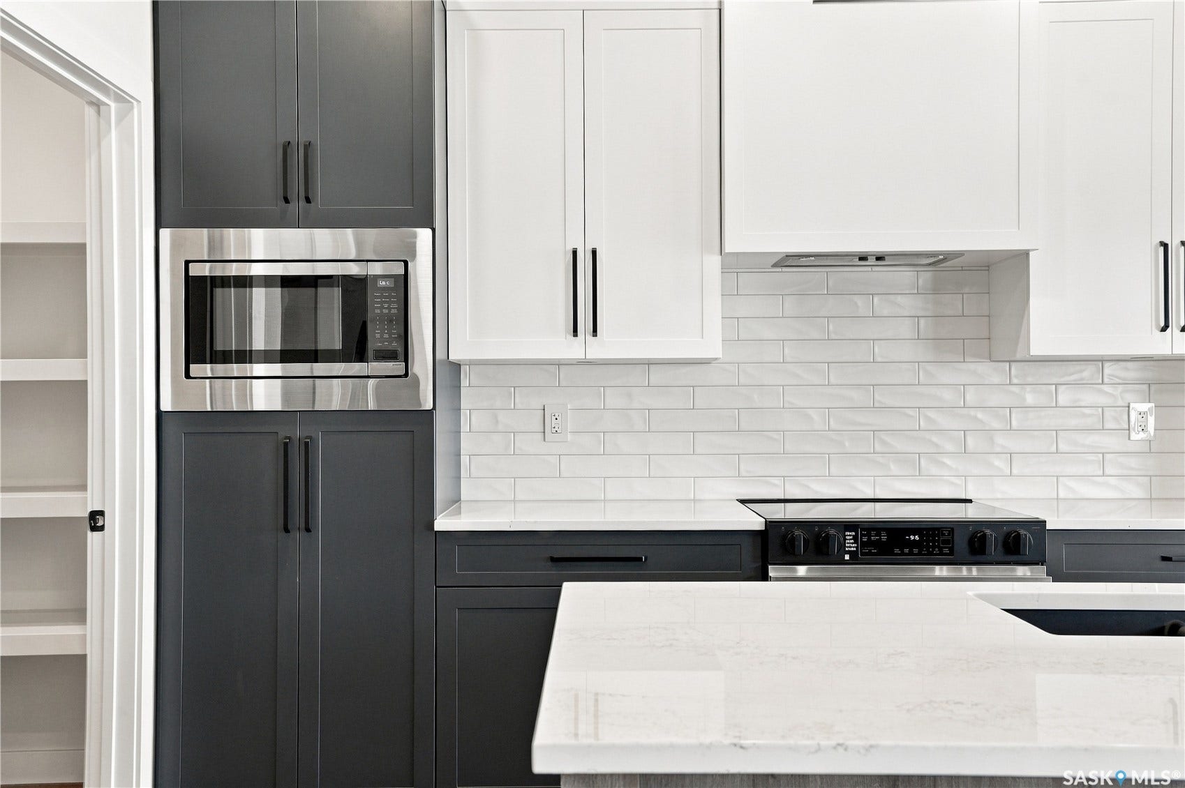 Two-tone cabinetry, built-in stainless steel microwave, electric cooktop, white subway tile backsplash, and light-toned countertops