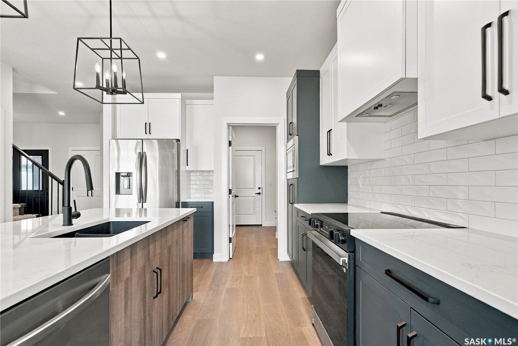 Spacious kitchen featuring an expansive island, stainless steel appliances, light wood-finish flooring, two-toned cabinetry, and white countertops