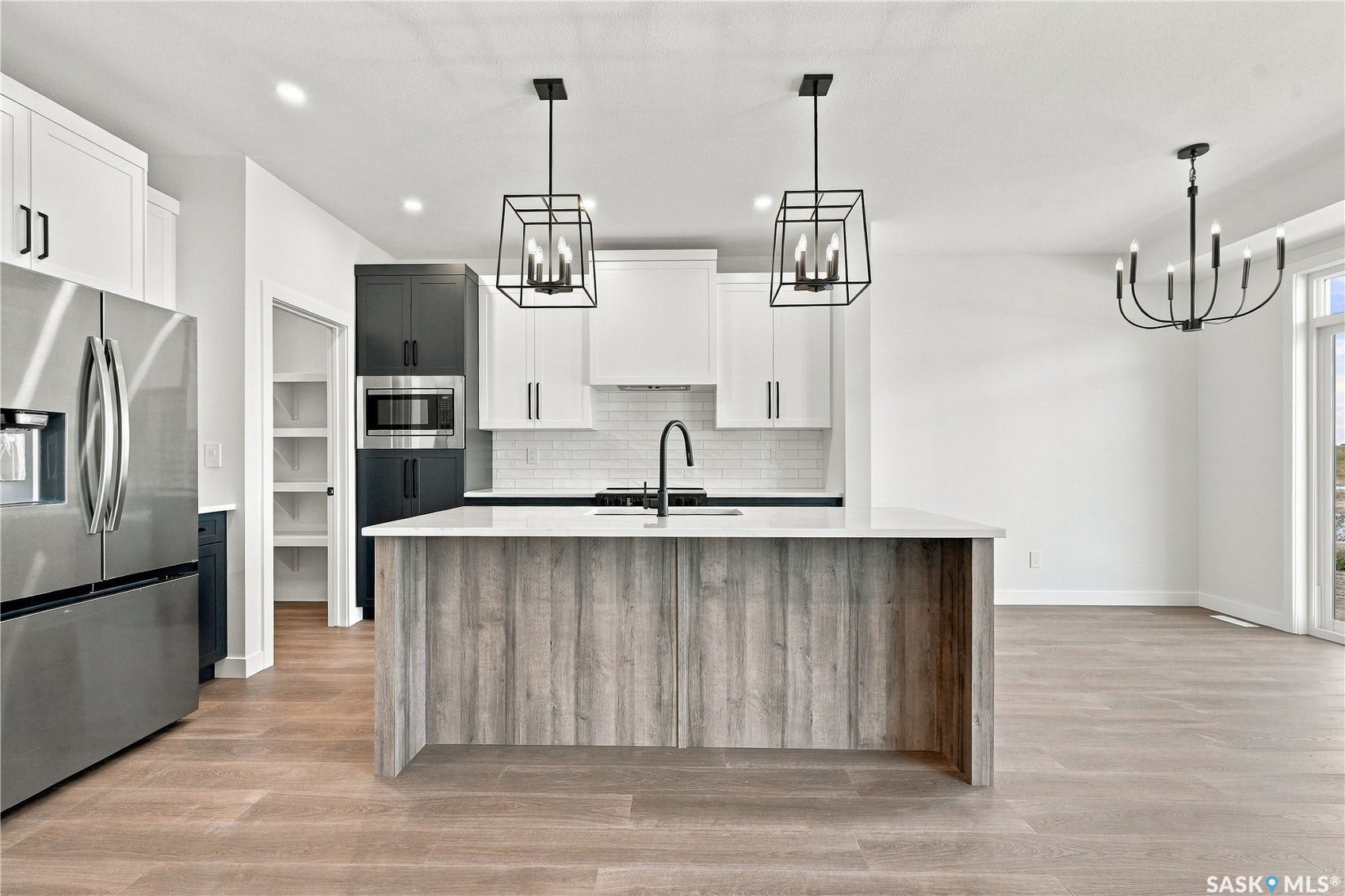 Modern kitchen featuring an island with a light-toned wood-finish base, stainless steel appliances, white cabinetry, and matte black lighting fixtures