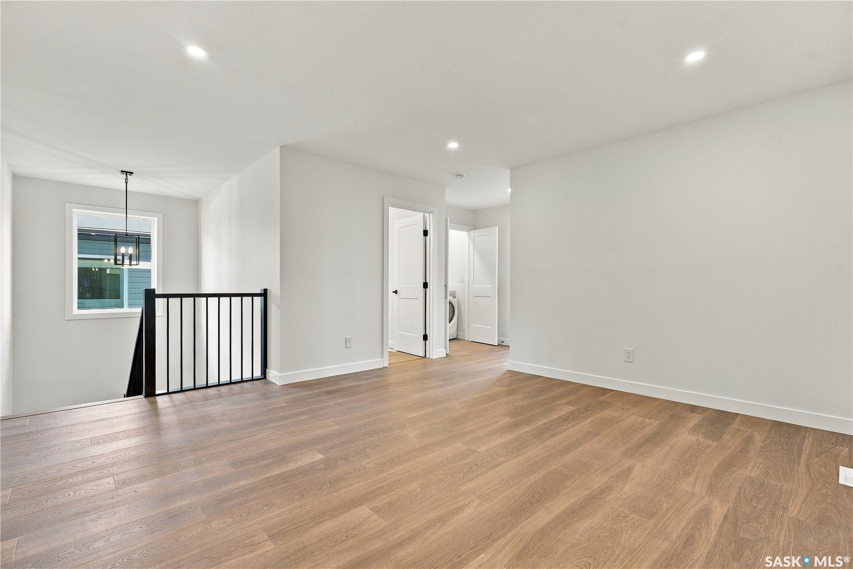 Light wood-finish flooring, recessed lighting, and a black metal railing