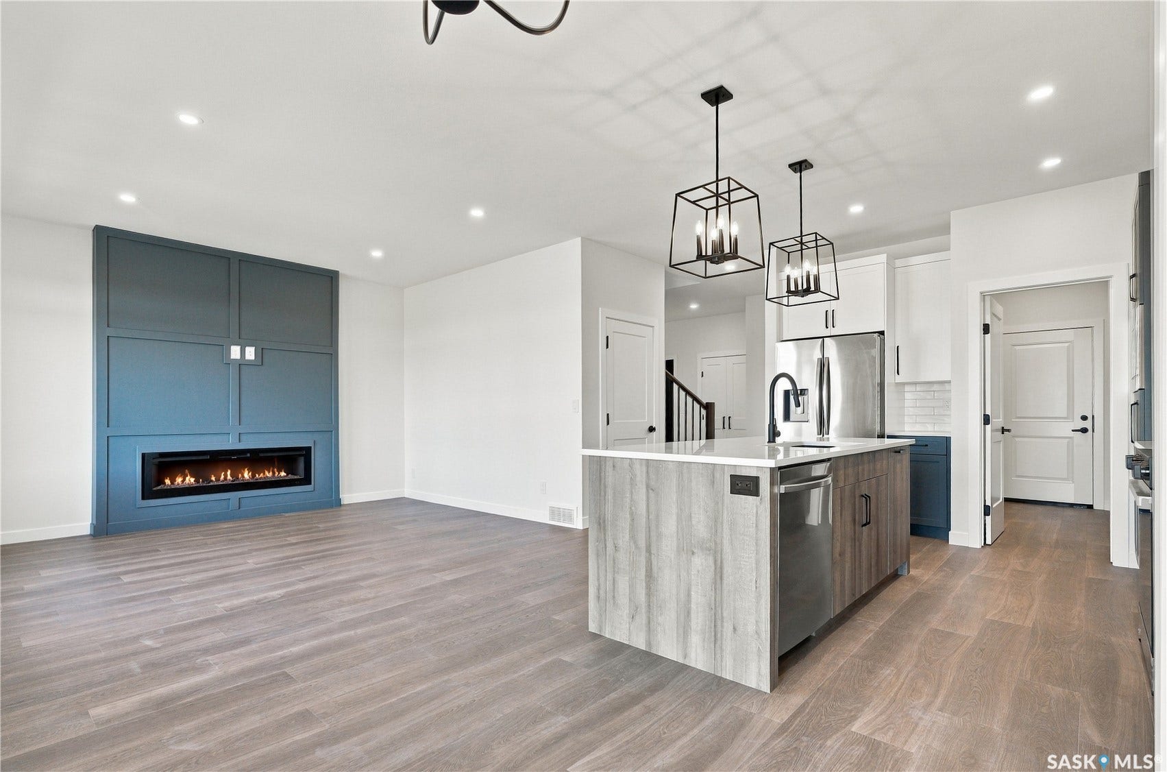 Open-concept living area featuring wood-finish flooring, a linear electric fireplace with custom paneling, a kitchen island with built-in dishwasher, and pendant lighting