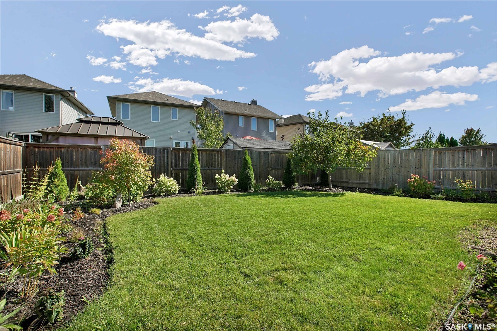 Expansive backyard featuring a manicured lawn, established perimeter fencing, landscaped garden beds, and mature trees