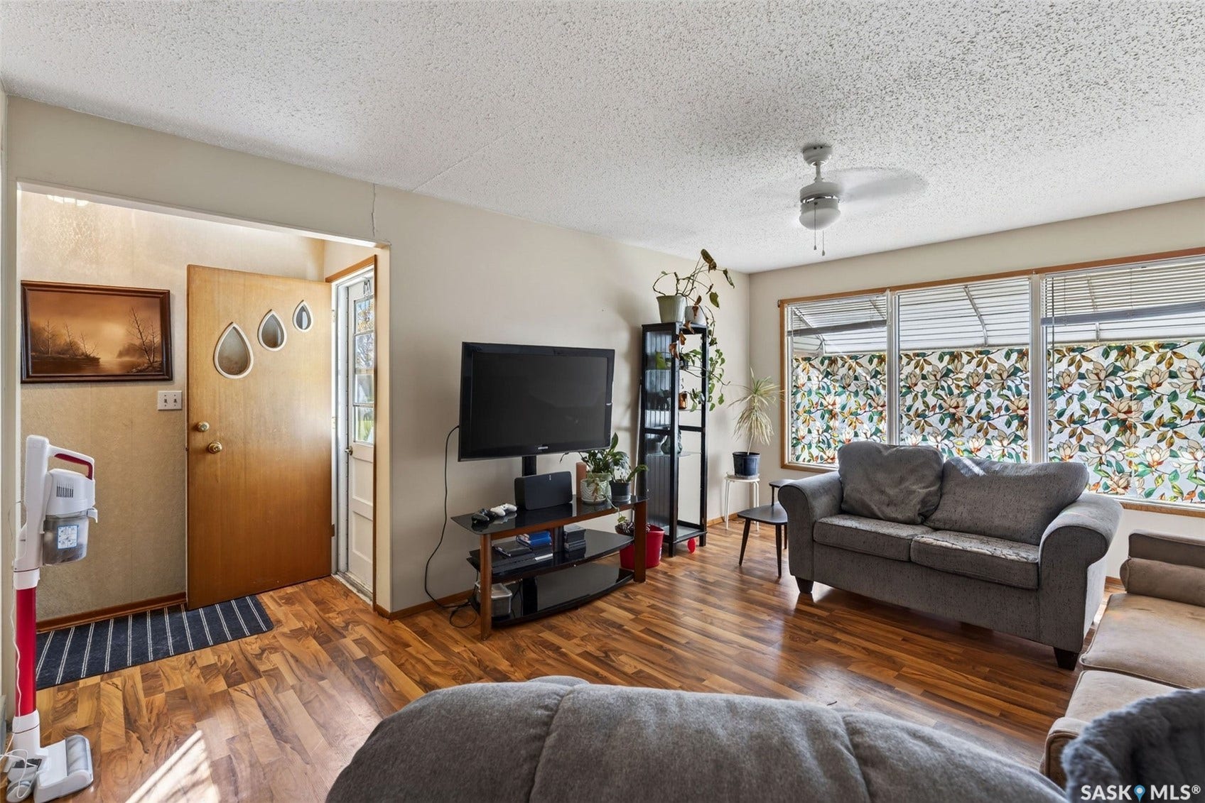 Wood-finish flooring throughout, featuring a functional ceiling fan and a wood-panel entry door