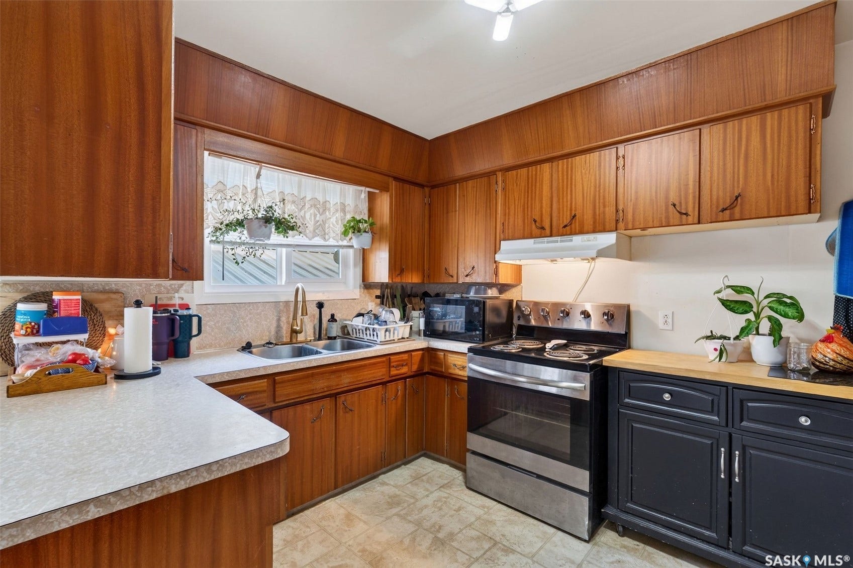 Wood-finish cabinetry and paneling, dual basin sink with brass-finish faucet, stainless steel range, and light-tone countertops