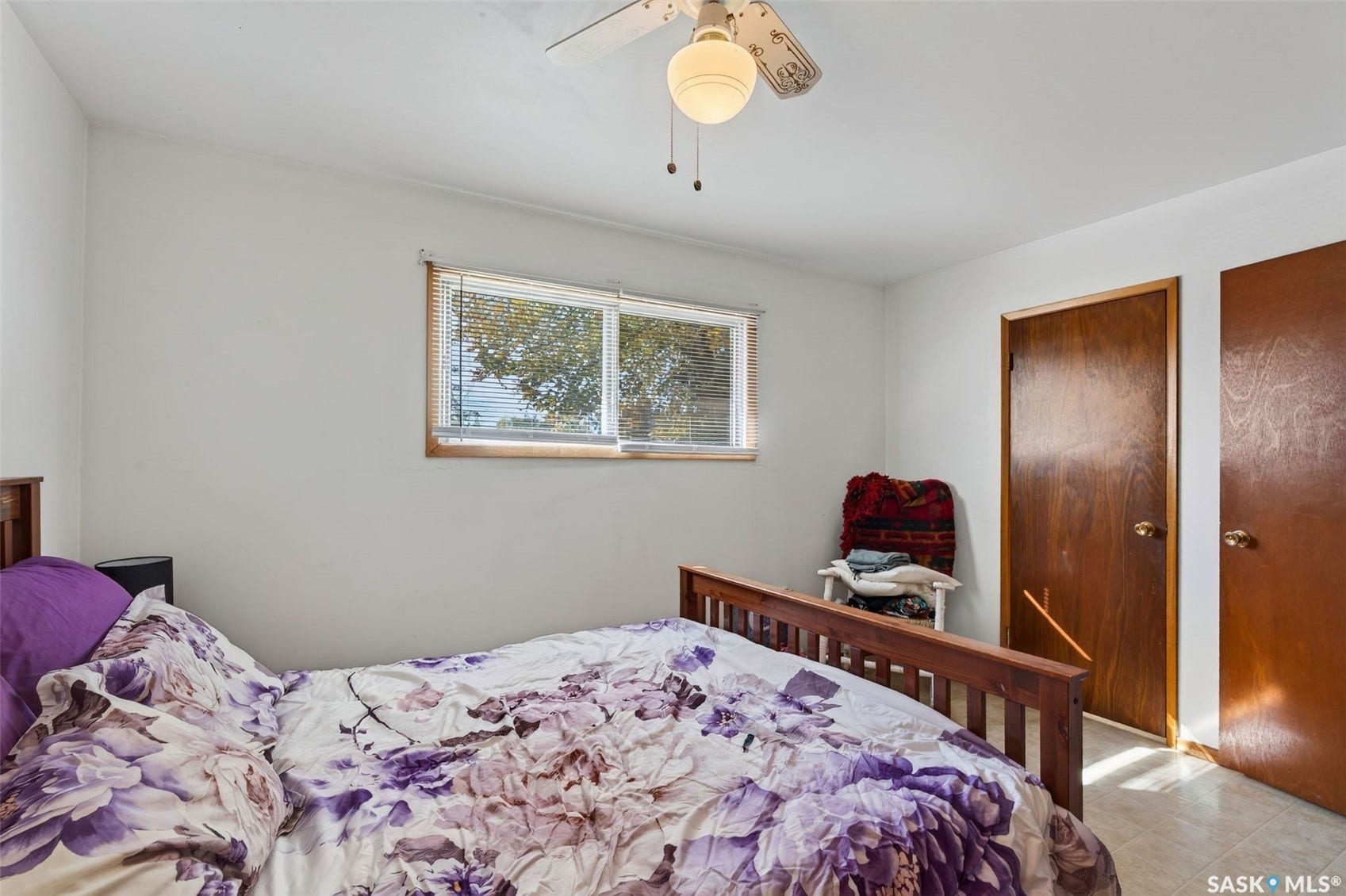 White walls with a light-toned ceiling, a window with wood-finish trim, a ceiling fan with integrated lighting, and two wood-finish doors