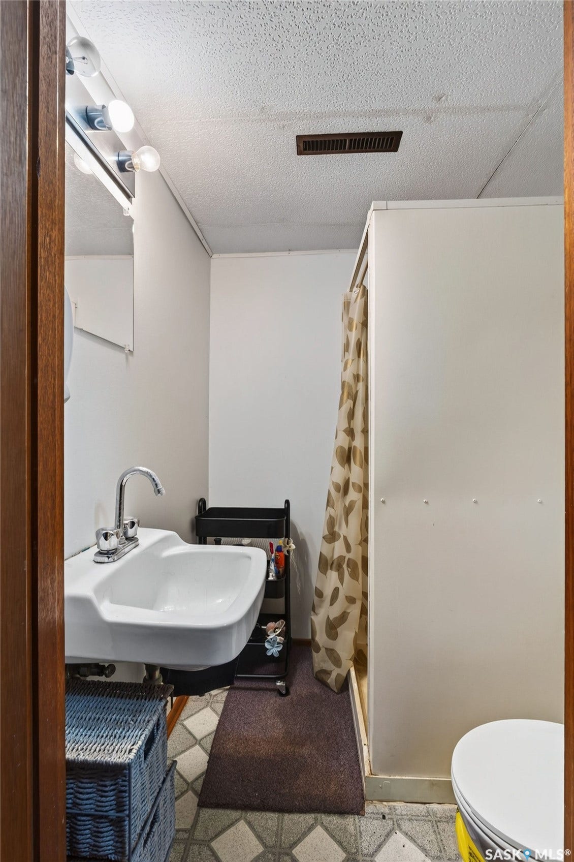 Pedestal sink with chrome faucet, enclosed shower stall, and patterned floor tile