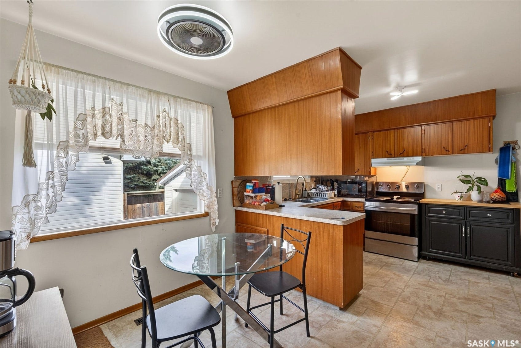 Kitchen featuring wood-finish cabinetry, stainless steel range and hood, light-toned tile flooring, and a large window