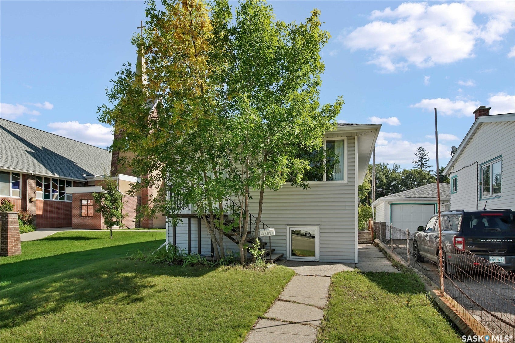Split-level exterior with light-colored siding, a paved walkway, and a landscaped front yard with mature trees