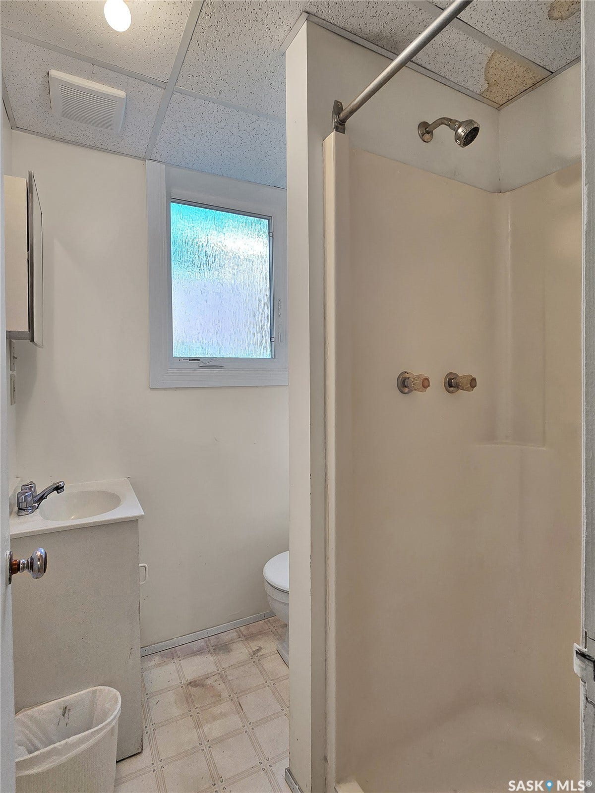 Bathroom featuring a single vanity, a toilet, a shower stall, and a window