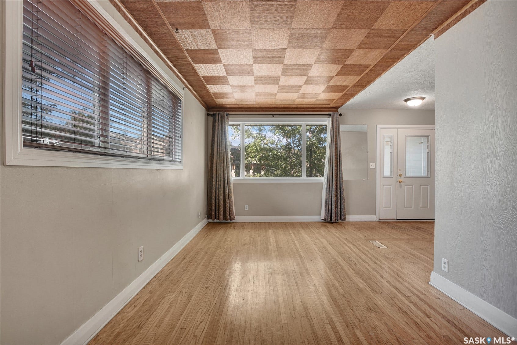 Hardwood flooring, checkerboard wood-paneled ceiling, large windows, double entry doors with decorative glass inserts, and neutral wall tones