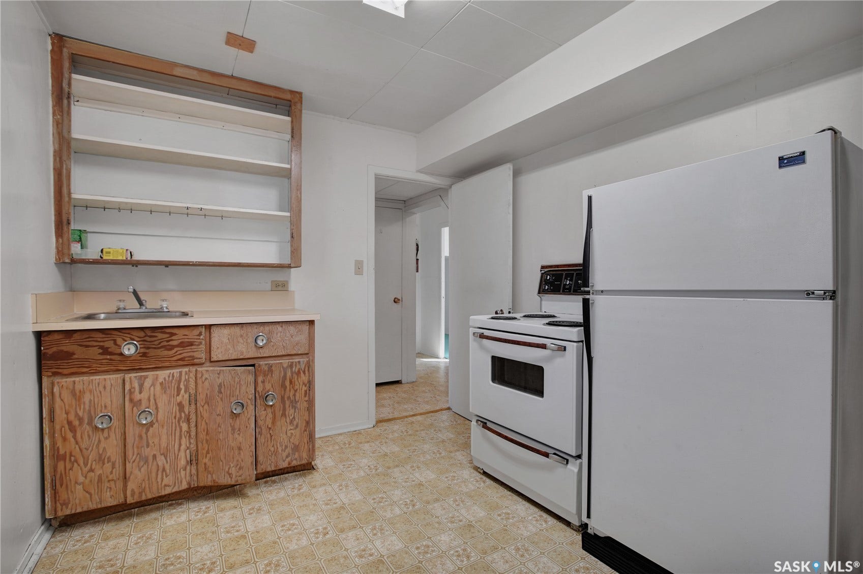 Kitchen area featuring a built-in sink, base cabinetry, upper open shelving, a freestanding range, and a refrigerator