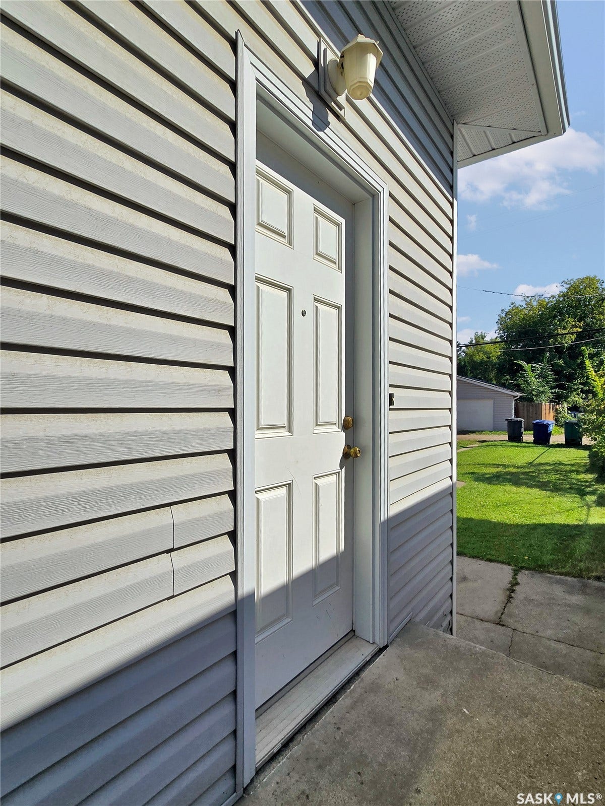 Gray horizontal vinyl siding with a paneled entry door and exterior sconce