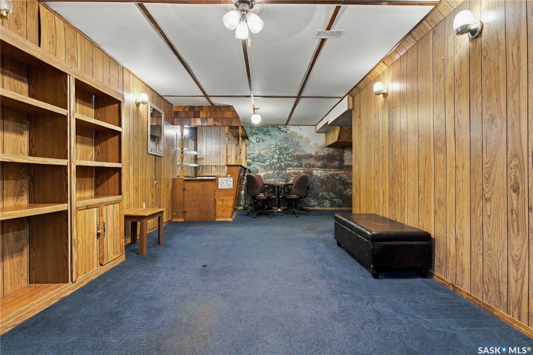 Wood-paneled room with built-in shelving, blue carpet, wall sconces, and a ceiling-mounted fan with integrated lighting